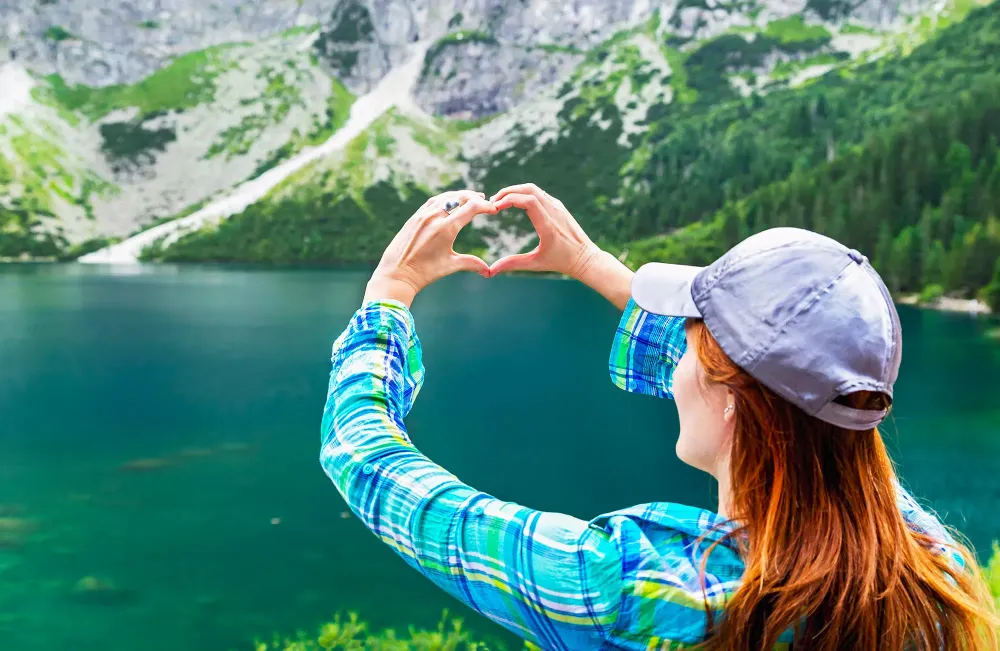 Girl make heart sign (shape of heart) on like, mountains background. In love with nature. Eye of the Sea lake (Morskie Oko). Tatra mountains. Poland.